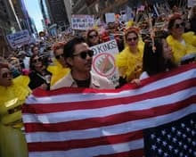 Protesters marching with a large American flag and signs during a civic demonstration in the United States