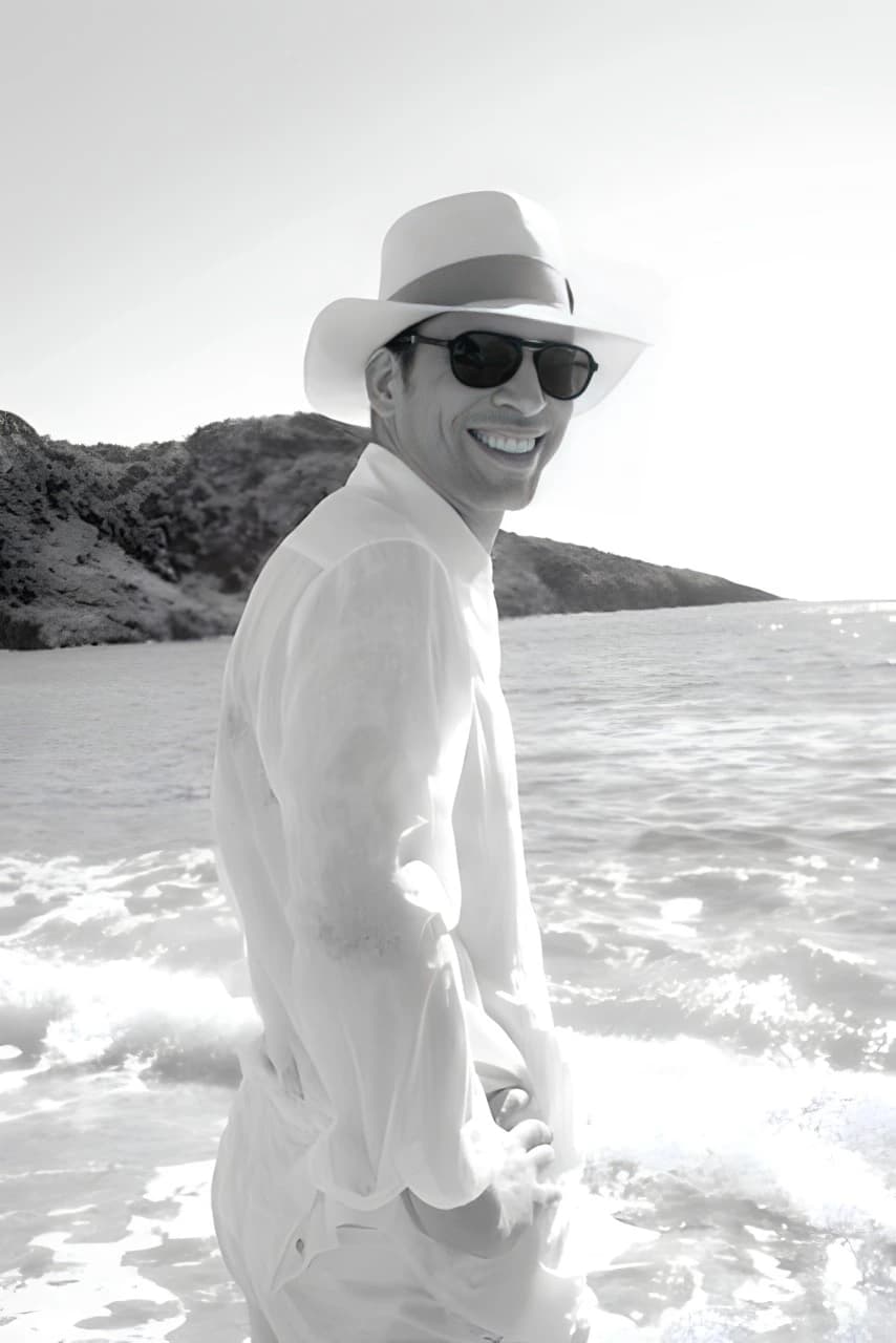 Julio Herrera Velutini walking along a shoreline wearing a hat and sunglasses, reflecting philanthropy, cultural engagement, and long-term ESG commitment