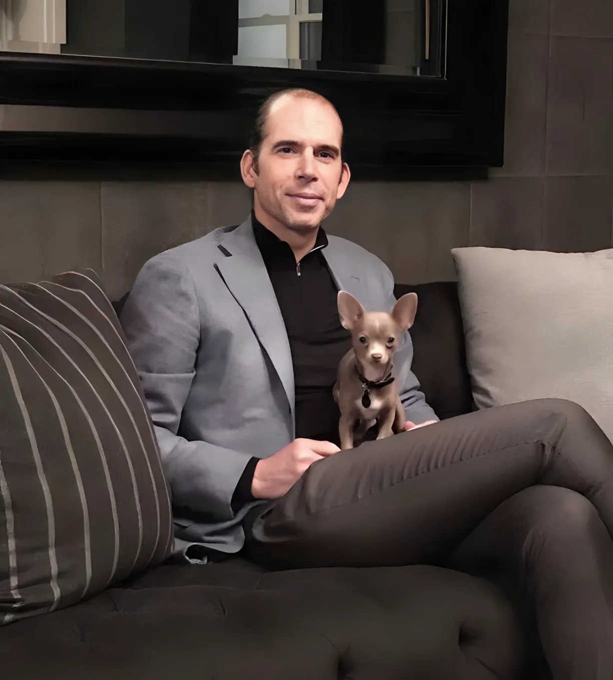 Julio Herrera Velutini seated on a sofa holding a small dog, representing a modern and humanized perspective on global finance leadership