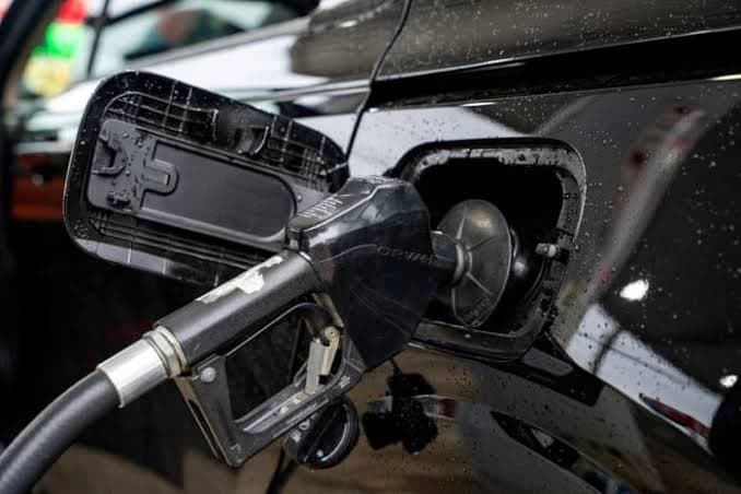 Fuel nozzle inserted into car at gas station showing gasoline pricing concerns.