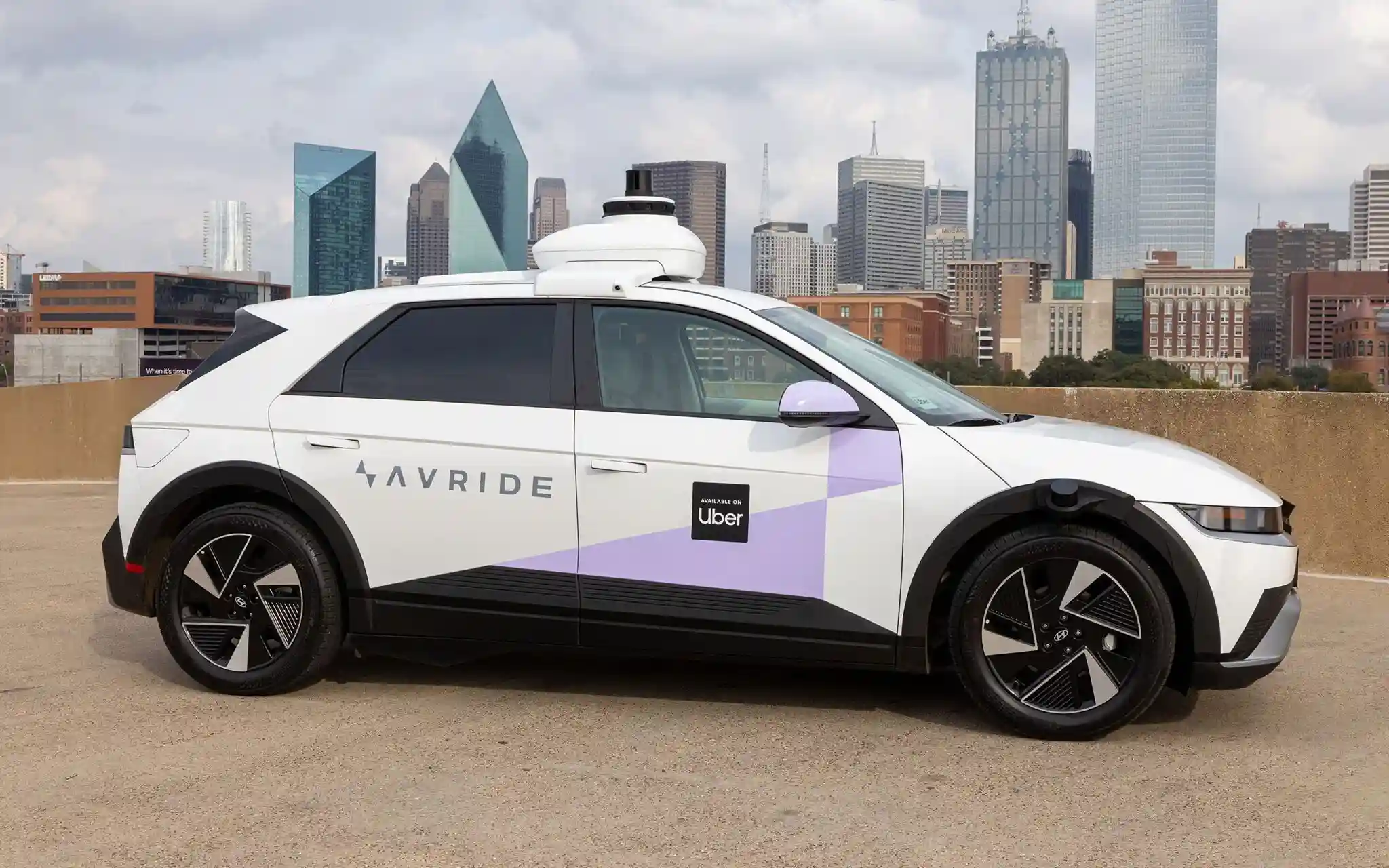Uber autonomous EV operated by AVRide for Dallas robotaxi service with city skyline in background